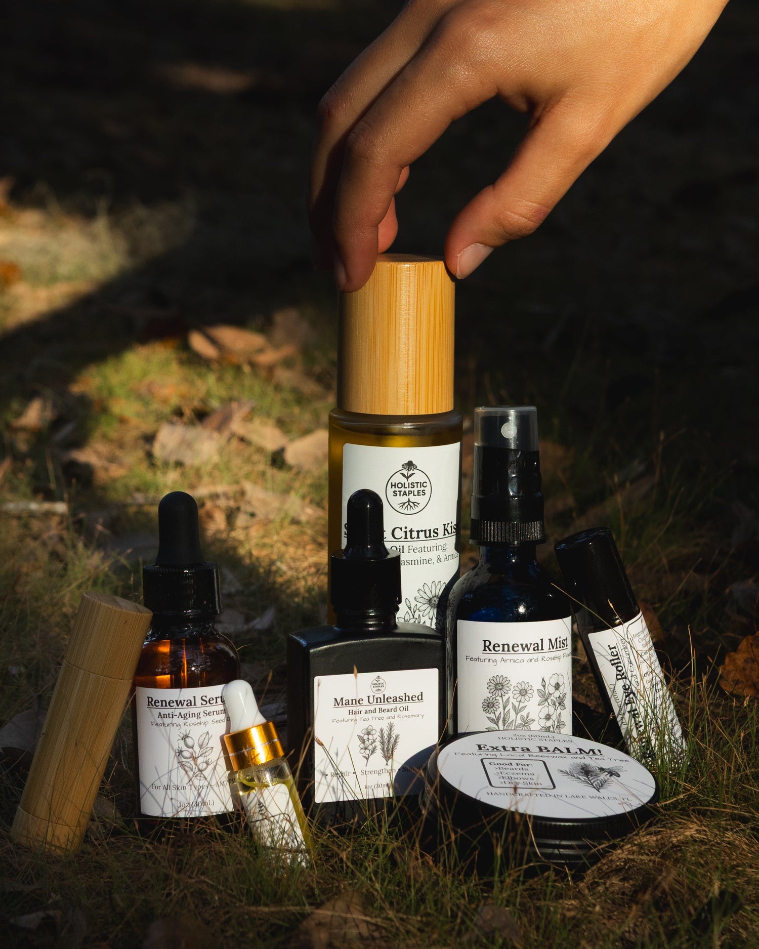 Collection of skincare products on a grassy surface with a hand reaching for one of the bottles.